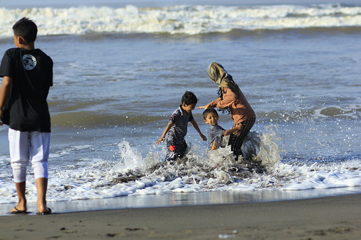 Yogyakarta, Indonesia, Feb 15, 2015. A young mother and two sons played waves until her clothes were soaked on the beach in Parangkusumo.
