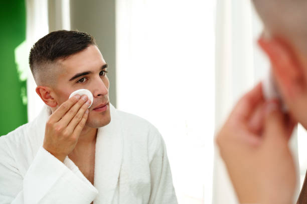 Handsome young man using cotton pad on his face in bathroom