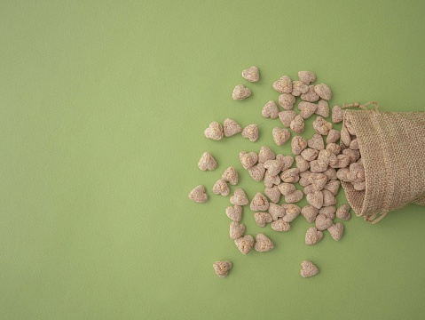 Extruded bran in the shape of a heart is poured out of a cloth bag onto a green background with space for text.