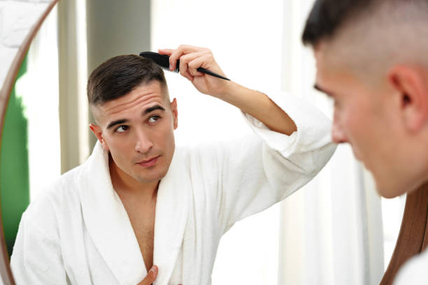 istock Handsome young man combing his hair while standing against mirror in the bathroom 2029494361