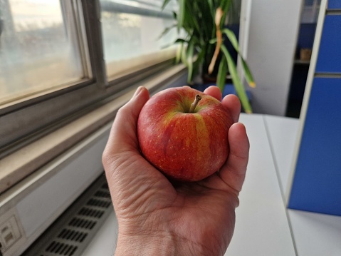 Hand holding apple indoors in the office.