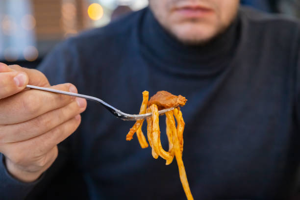 Lagman noodles on fork. man eats bucatini noodles. noodle soup with meat