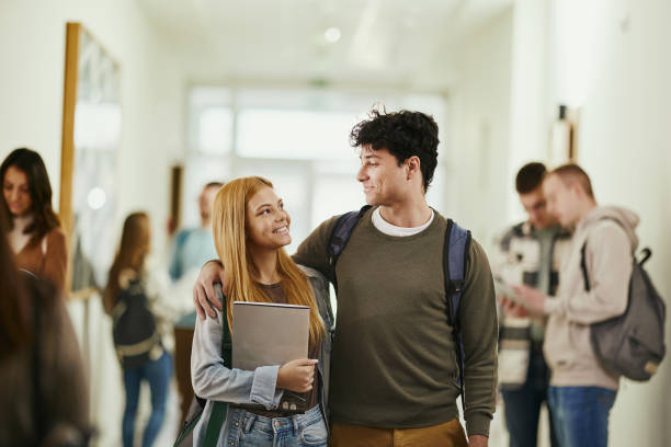 istock Happy college couple talking while walking embraced in a hallway. 2029591502