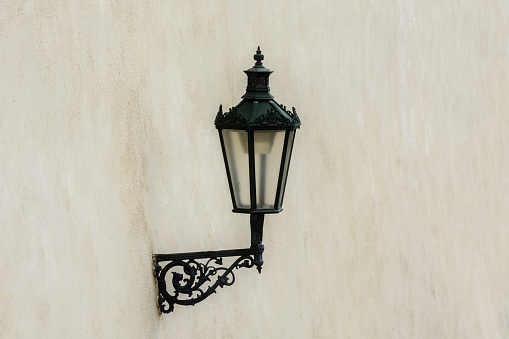 Street lamp on a black iron bracket against a beige wall background.