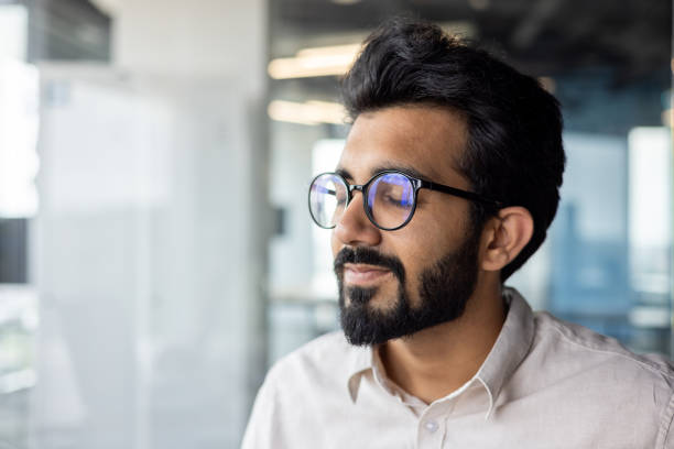 istock Man with black hair, glasses beard smiles while looking out window 2029607134