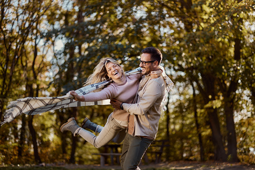 Playful couple having fun while spinning during autumn day at the park. Copy space.