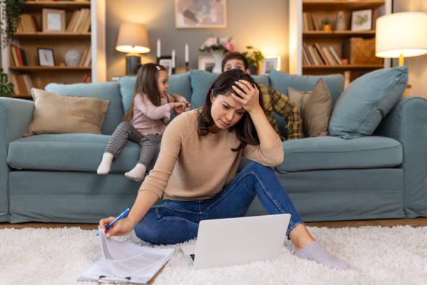 istock Tired young mother sitting on sofa and working with laptop and documents while little kids, her daughter and son are having fun on the sofa and making noise 2029607701