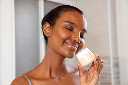 Eyes Closed Beautiful Smiling Black Woman Holding a Cream Closer to her Face in the Morning, Italy