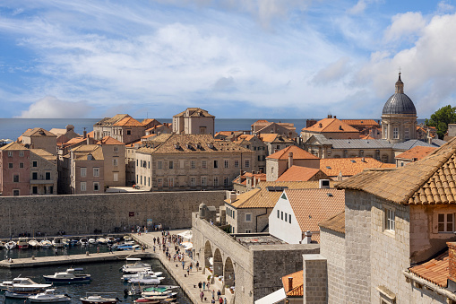 Dubrovnik, Croatia - June 27, 2023: View from City Walls of the picturesque medieval Old Port ( Stara Luka) by Adriatic Sea with moored ships. Dome of Dubrovnik Cathedral