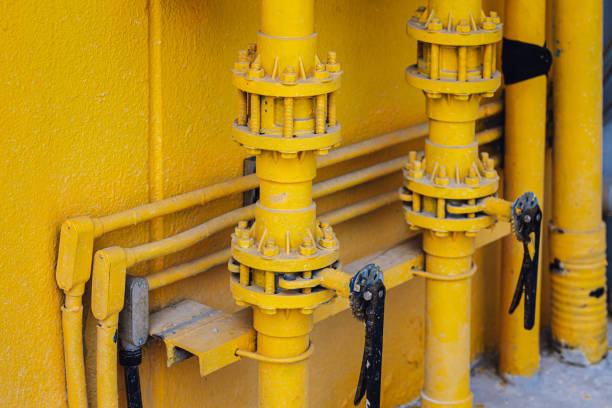 A close up shows a red industrial valve and pipeline system outdoors in daylight, horizontal view.