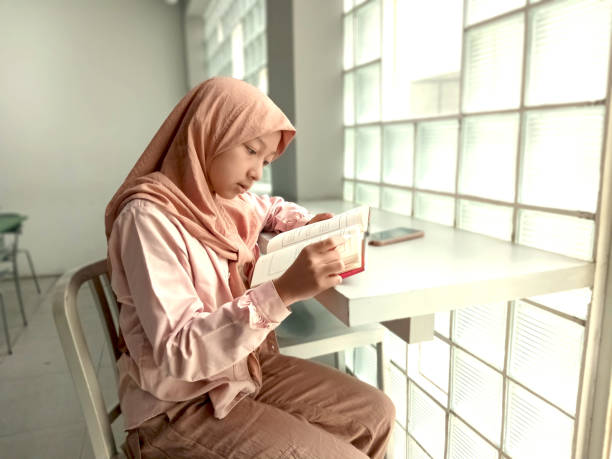 Two beautiful hijab ladies learning together by reading a book and using laptop