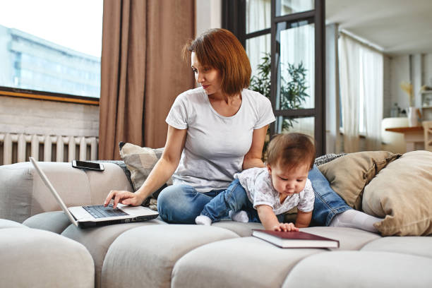 istock A woman with a child at a laptop sitting on a sofa. Work at home, freelancer, work during maternity leave for remote access. 2029639720