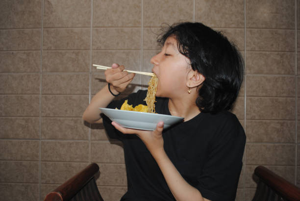 Asian girl is enjoying noodles at home.
