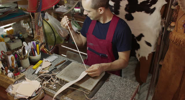 Craftsman in apron doing leather work in craft studio workshop. SME business.