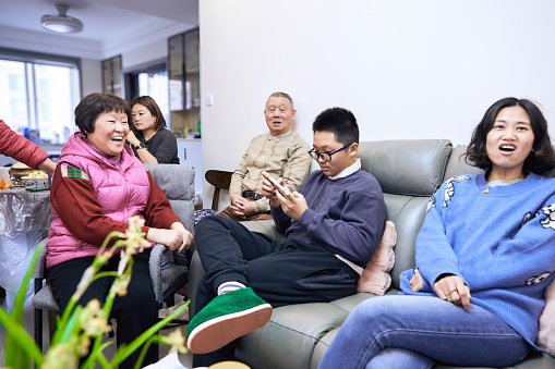 three generation asian family reunion in living room during chinese new year, gatheirng, talking and eating snacks