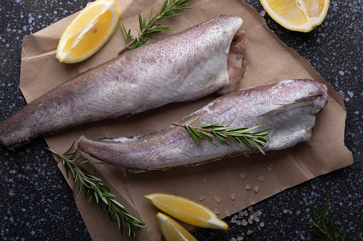 Fresh raw fish adorned with lemon and rosemary, presented on a dark, textured background, perfect for culinary themes and gourmet cooking content
