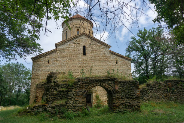 istock Ancient church in the forest. Bricks and stone wall. Partially destroyed arched extension at the entrance. Orange tiled roof, grass lawn. 2029701553