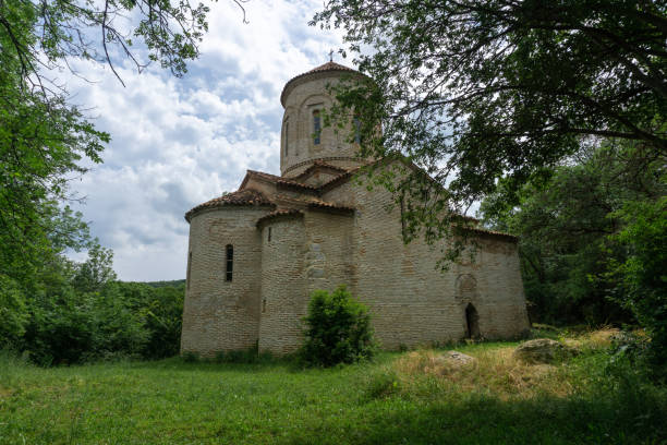 istock Ancient church in the forest. Bricks and stone wall. Partially destroyed arched extension at the entrance. Orange tiled roof, grass lawn. 2029704209
