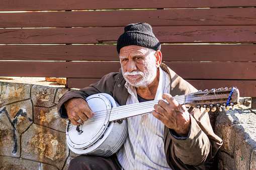 Antalya, Turkey - November 15, 2022: An elderly man with handcrafted stringed instrument on an urban sidewalk.