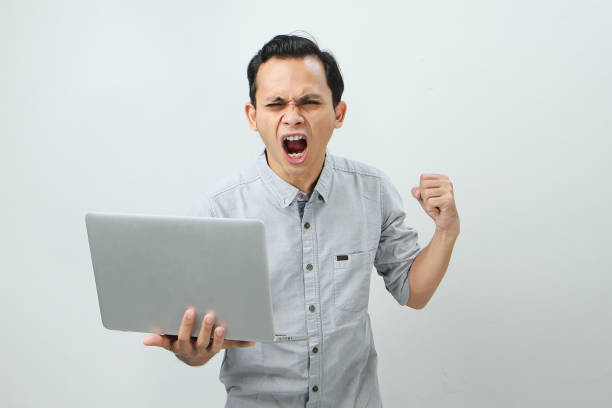 angry mad asian man holding laptop computer on isolated background