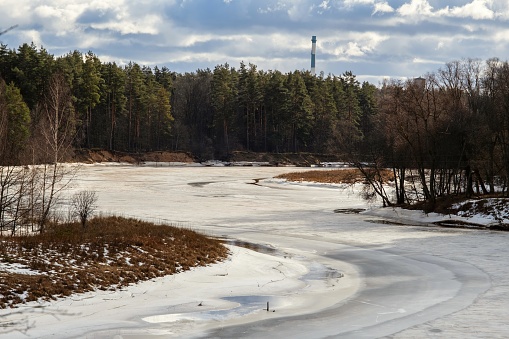 A frozen river in a snowy landscape with an industrial tower in the background