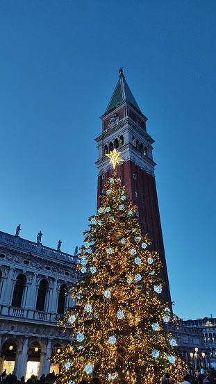 bell tower of Piazza San Marco in Venice with Christmas tree and lights at dusk, shot from below with intense blue sky