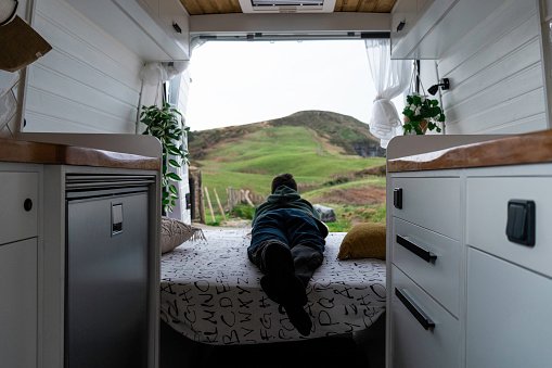 Child observes the landscape lying in a vintage Nordic style camper van.\nConcept van life, lifestyles, people