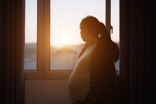 Silhouette of pregnant woman by window