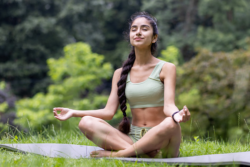 A young Indian woman in a green tracksuit performs yoga in a tranquil park setting, exhibiting grace and wellness.