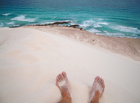 Woman feet on sand dunes overlooking the idyllic crystal sea, Socotra, Yemen