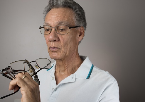 An elderly man holding up a bunch of eyeglasses