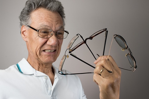 An elderly man holding up a bunch of eyeglasses
