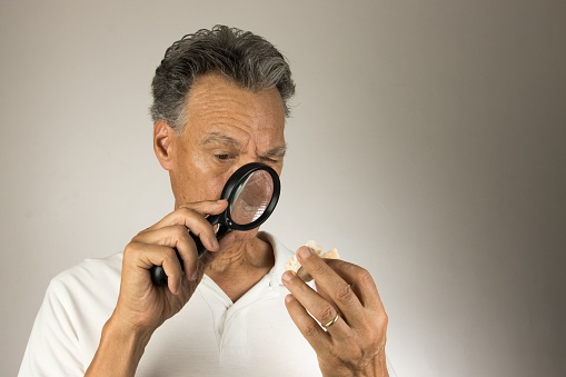 An elderly Hispanic man examining a tooth mold with a loop