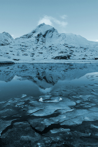 Winter landscape of freezing lake and mountain reflection with ice blocks on the water surface, Lofoten, Norway