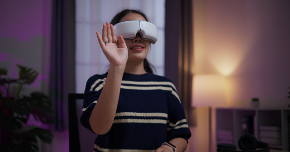 Selective focus, Cheerful young woman wear glasses of virtual reality while touching air sitting on table in the living room at home, VR technology, Innovative