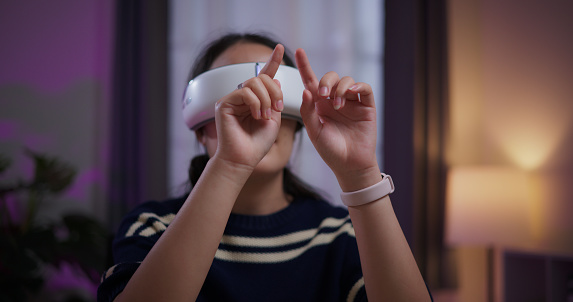Selective focus, Cheerful young woman wear glasses of virtual reality while touching air sitting on table in the living room at home, VR technology, Innovative