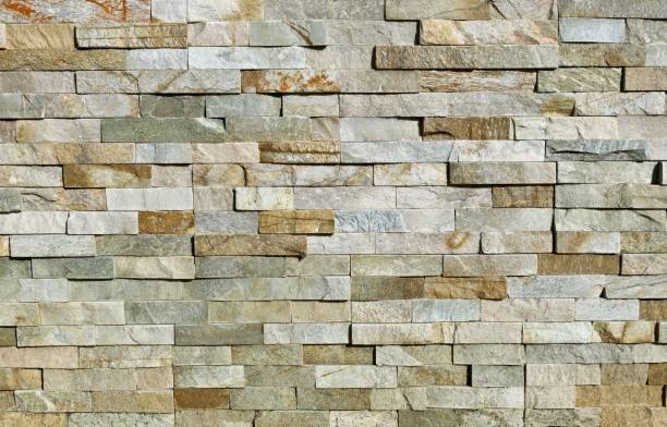 muro de revestimiento de piedra hecho de ladrillos apilados rayados de rocas. los colores principales son marrón, gris, verde y blanco. revestimiento de paredes externo - recubrimiento capa exterior fotografías e imágenes de stock