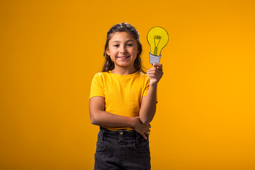 Portrait of smiling child girl holding paper bulb above head. Success, motivation, winner, genius, idea concept