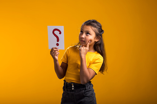 A portrait of thoughtful kid girl holding question mark card. Children, idea and knowledge concept