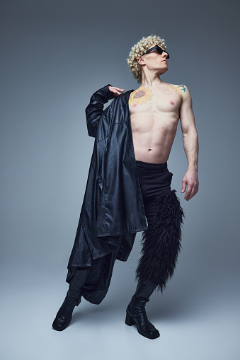 Full length portrait of young handsome shirtless man with athletic body posing in black outfit against grey studio background. Concept of fashion fusion, art, uniqueness, self-expression. Ad