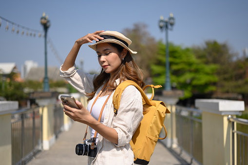 Attractive female traveller using mobile phone on bridge with scenery view of river and blue sky.