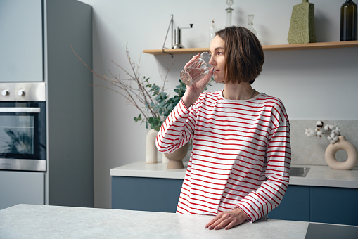 Attractive woman stands alone on the kitchen and drinking still water