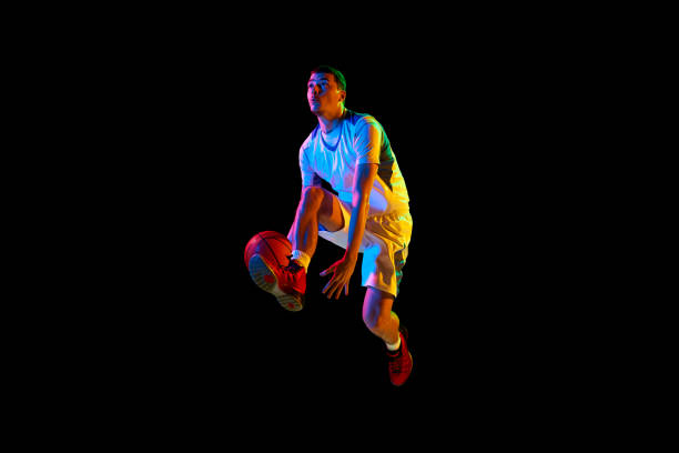 istock Dynamic portrait of young athlete man training basketball techniques against black studio background in mixed neon light. 2029872990