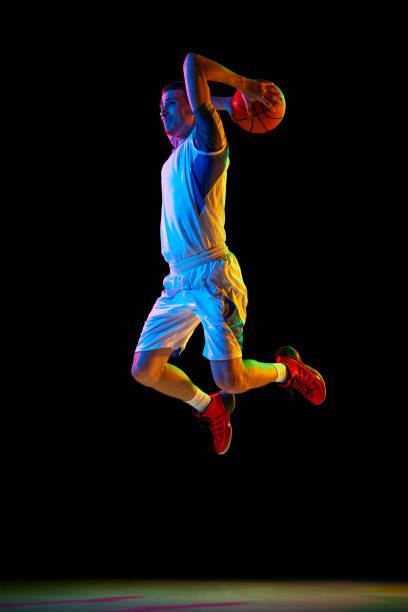 istock Basketball player doing layup to basket in action against black studio background in mixed neon light. Dynamic shot. 2029872997