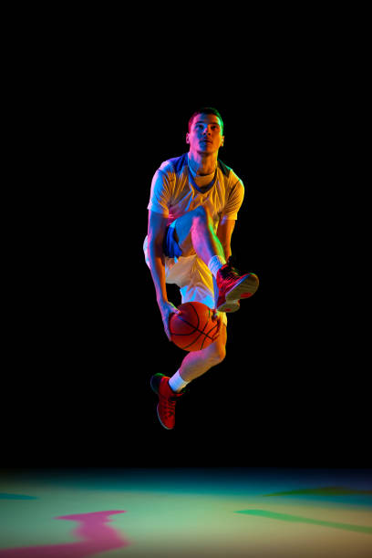 istock Concentrated athlete man, basketball player dribbling against black studio background in mixed neon light. Model training in action 2029873006