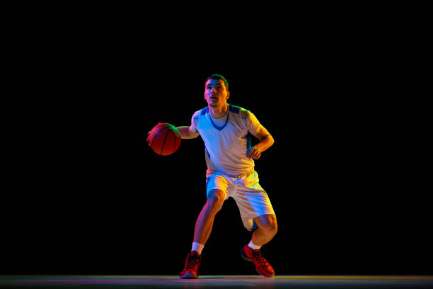 istock Focused athletic man, basketball player dribbles ball with one hand against black studio background in mixed neon light. 2029873013