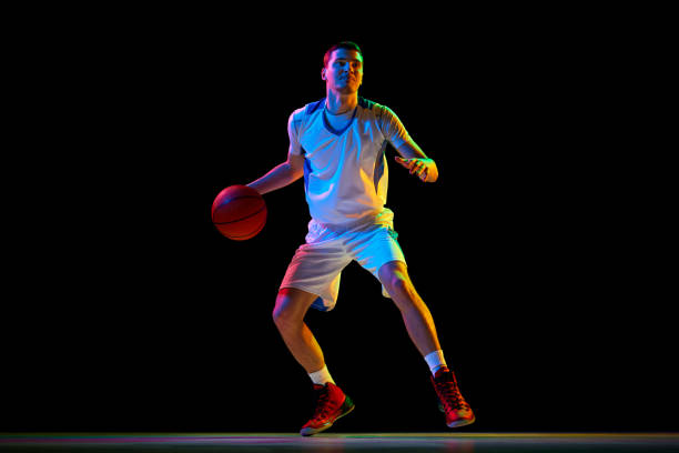 istock Focused basketball player, performs double ball technique in motion against black studio background in mixed neon light. 2029873015