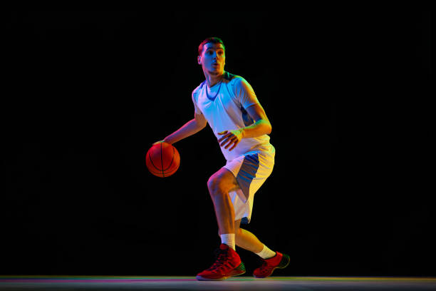 istock Young, focused basketball player performs combined ball-handling technique against black studio background in mixed neon light. 2029873017