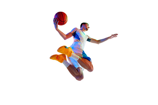 Basketball player in high-flying makes powerful dunk in motion against white studio background in neon light. Low angle. Concept of professional sport, energy, match, championship, tournament.