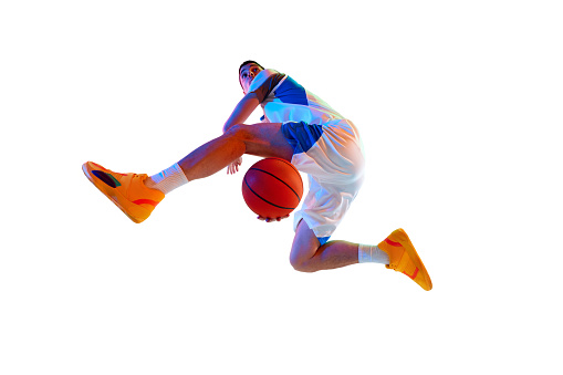 Low angle view. High-flying basketball player performing dunk in motion against white studio background in neon light. Concept of professional sport, energy, strength and power, match, tournament.